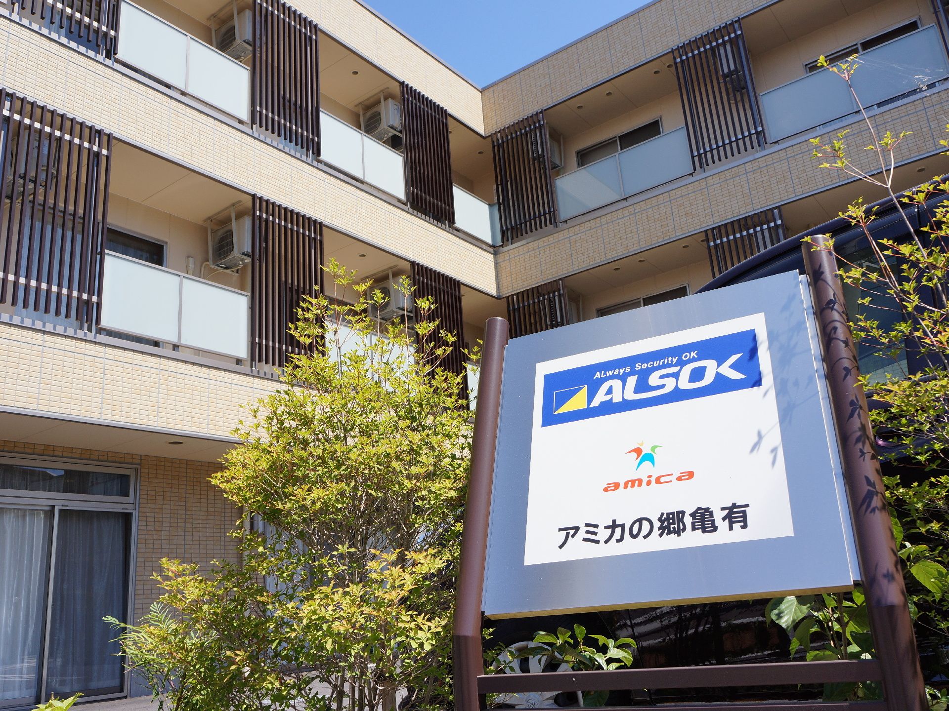 植栽のスペースに設置されている施設の表示板である。文字が大きくシンプルな表記となっているため分かりやすい。