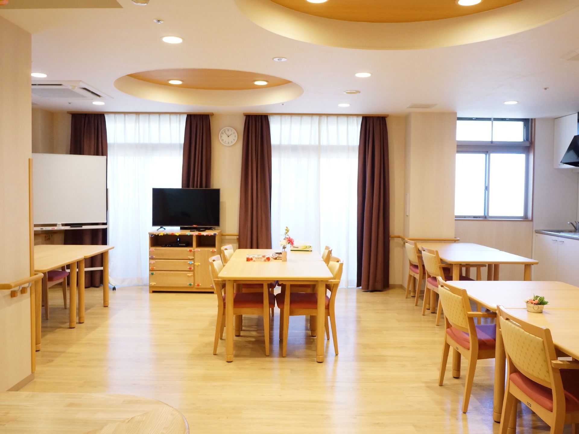 食堂の天井が、デザイン性のある形や照明に作られている。時計、テレビやホワイトボードなども置かれている。