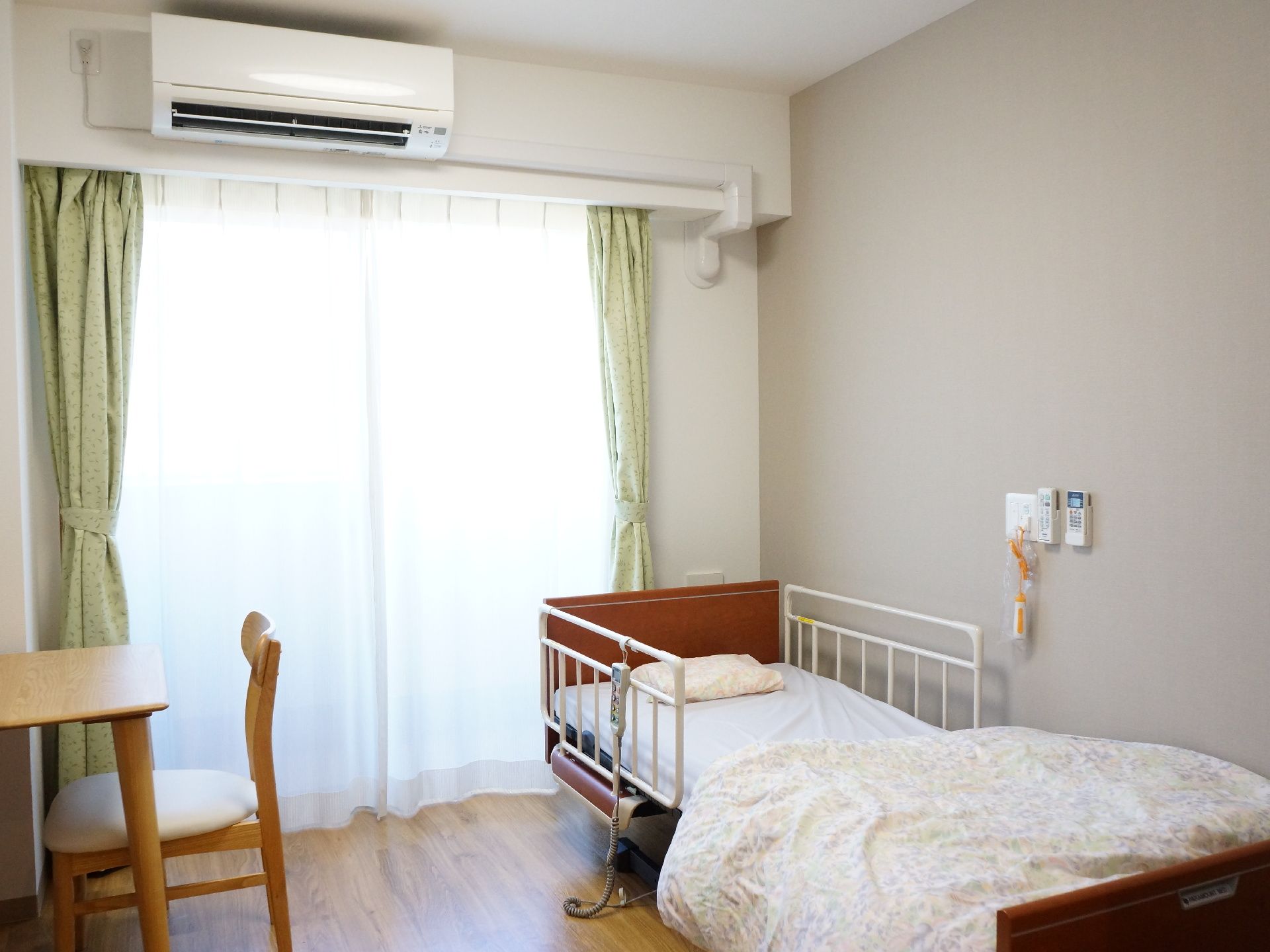 部屋には大きな窓があり、日差しが良く入る。電動介護ベッド、エアコン、ナースコールなどが設けられている。