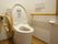 各部屋のトイレである。木目調で、壁には手すり、緊急用のコールボタン、洗浄機能付き便座が設置されている。