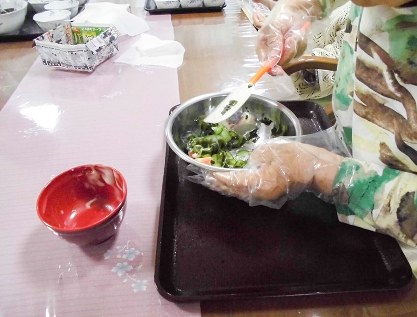 ビニール手袋をして、ボールに入れたきゅうりとわかめをあえる様子