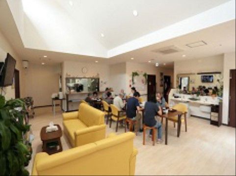 リビングで食事をとる入居者様。広い空間に黄色いソファと黄色い椅子を配置し、明るい雰囲気のリビングになっている。