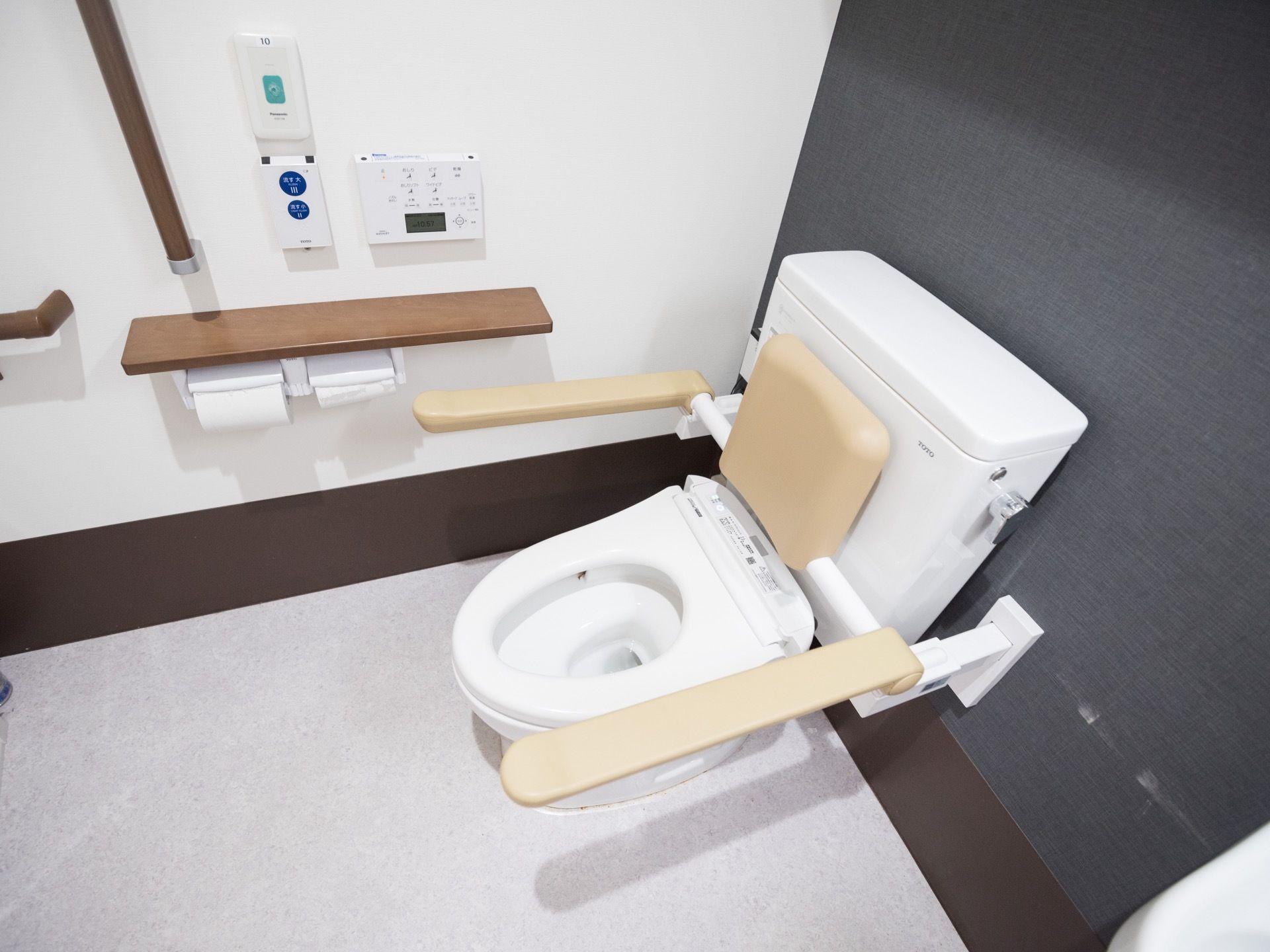 便器の両脇に手すりが設置されており、背中側にもクッションがある。壁には、ペーパーホルダーと手すりが取り付けられている。