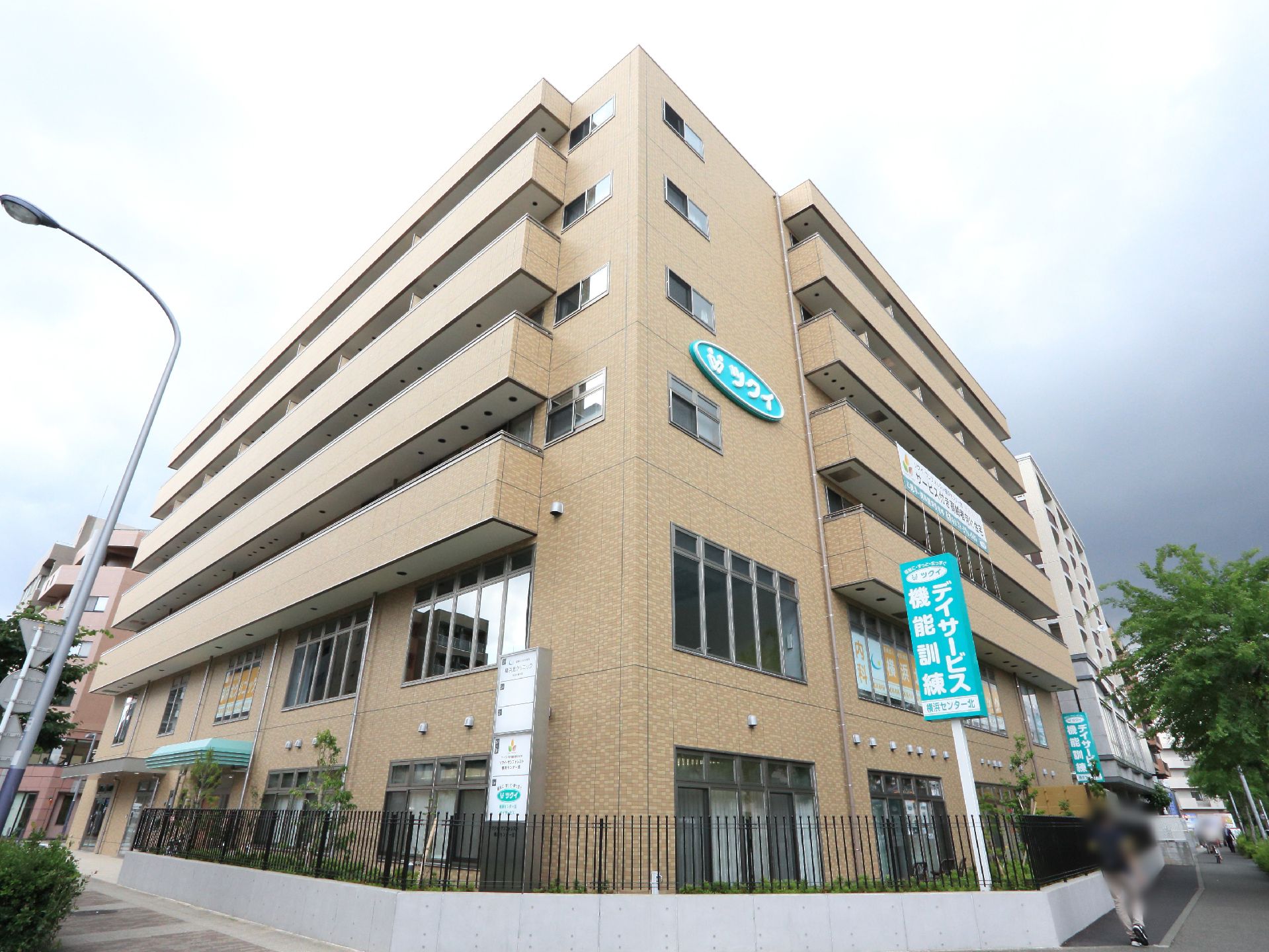 角地に立つ茶色の建物で3階から7階部分にテラスがついている。黒のフェンスと白い壁面で囲まれており壁にはし説明が入っている。
