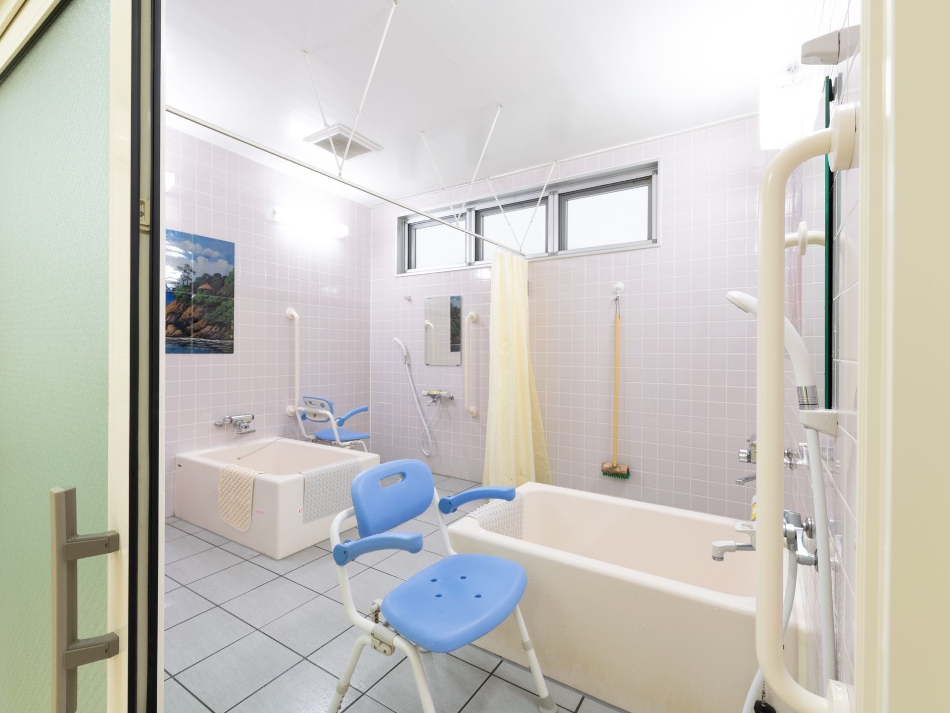 広々とした浴室には、中央に白色のカーテンが掛けられている。両端には、水色の補助椅子が１脚ずつ置かれている。