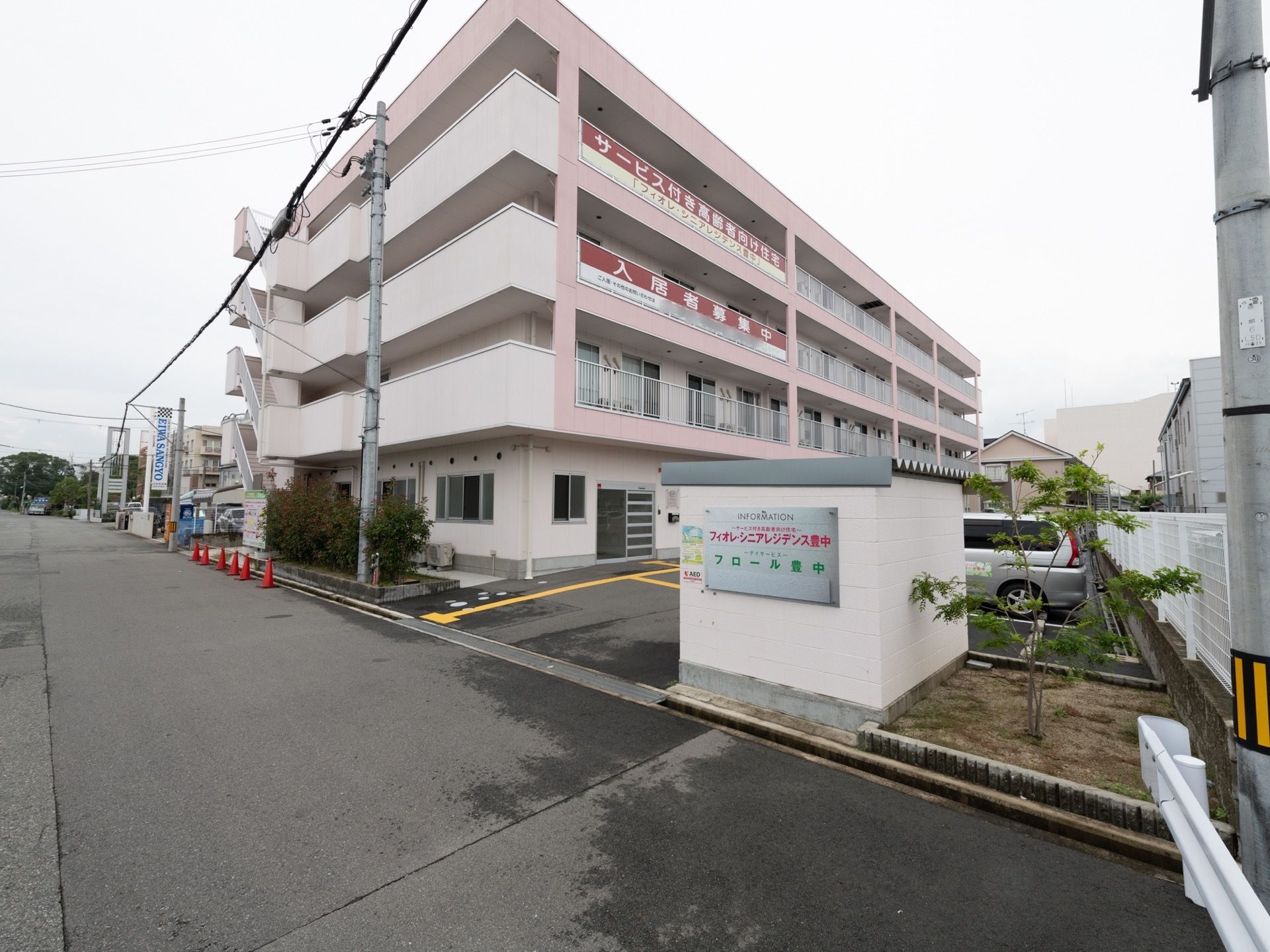 施設は４階建てで、薄いピンク色の外壁で統一されている。入口には、施設名の書かれたシルバーの表札が設置されている。