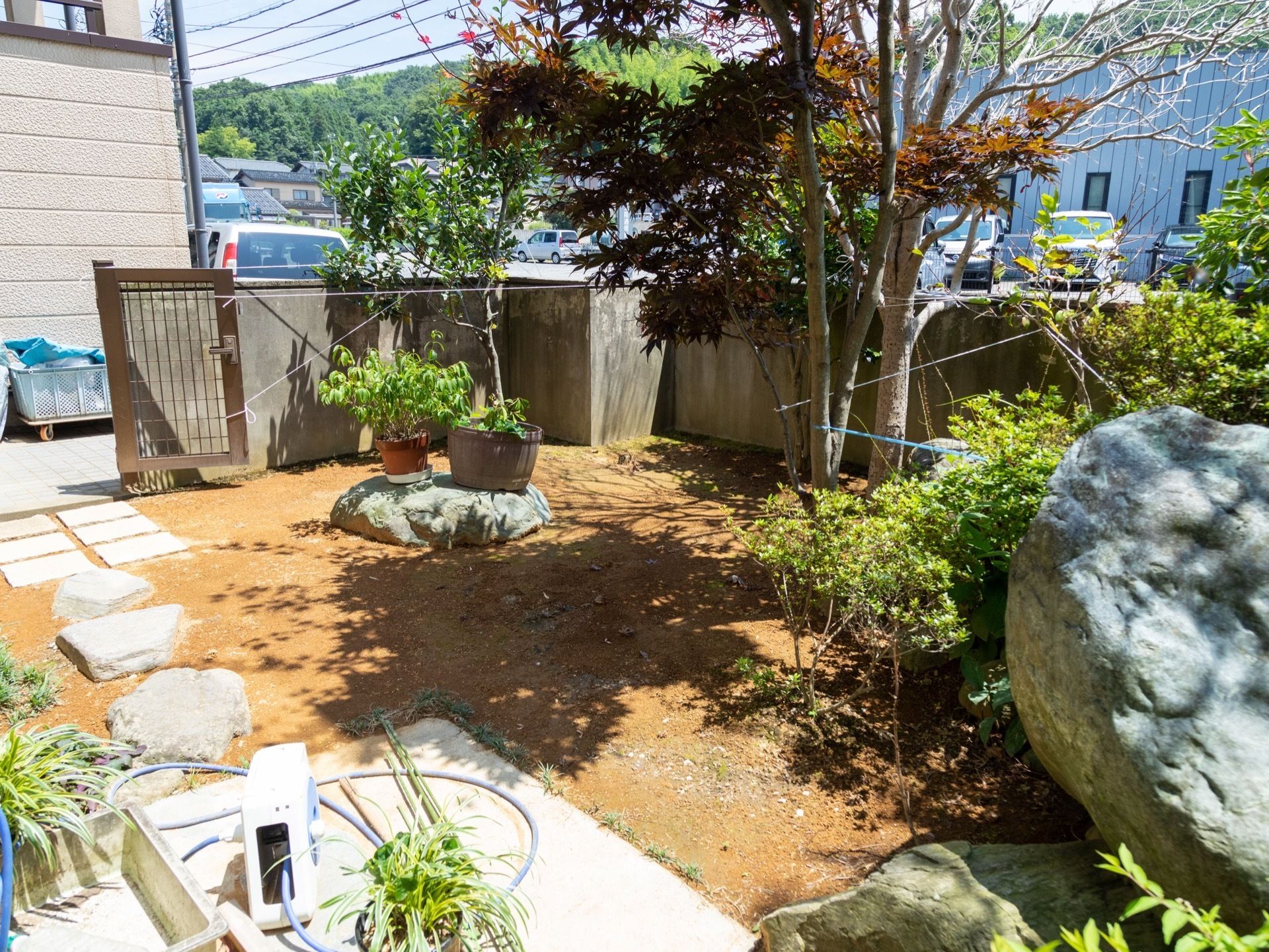 施設の敷地内に整備されている庭園の様子。いくつかの木が植えられており、水道には水まき用のホースが取り付けられている。