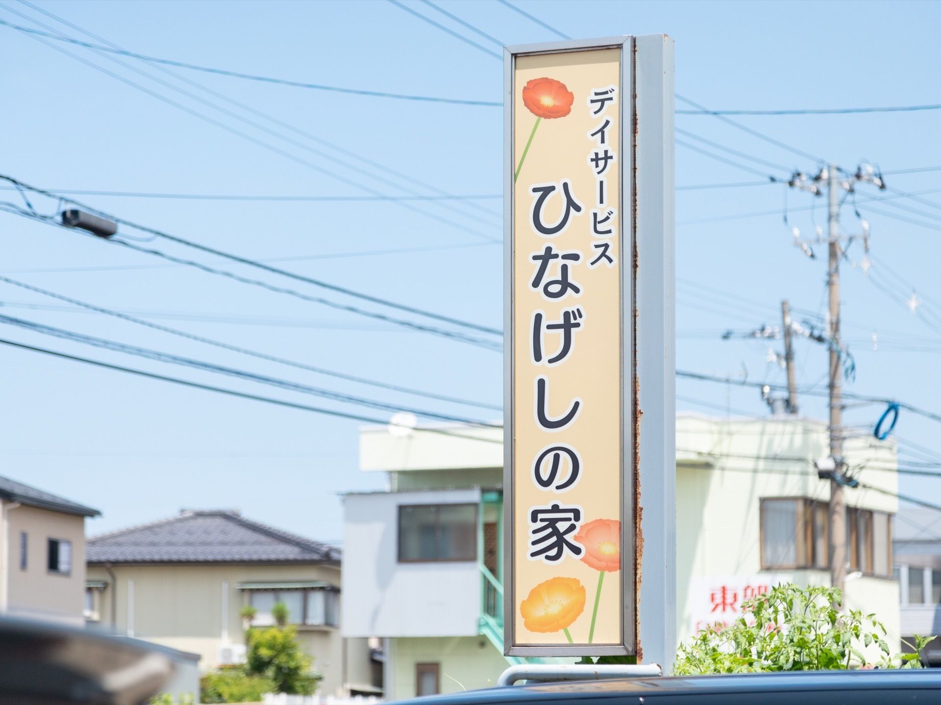 施設に面した大通りから見えるように立てられている看板。クリーム色で、花のイラストと施設名が書かれたデザインとなっている。