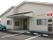 白い外壁の1階建て建物で、駐車場は建物の横に設けられている。玄関の横にはヘルパーステーションの出入り口がある。