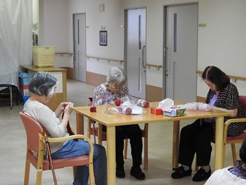 机を囲んで話しながら、熱心に編み物に取り組むご入居者様