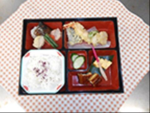 赤いチェックの風呂敷の上に、弁当箱が置かれている。天ぷらがメインのお食事で、豊富に野菜も使われているので、彩りもきれいである。