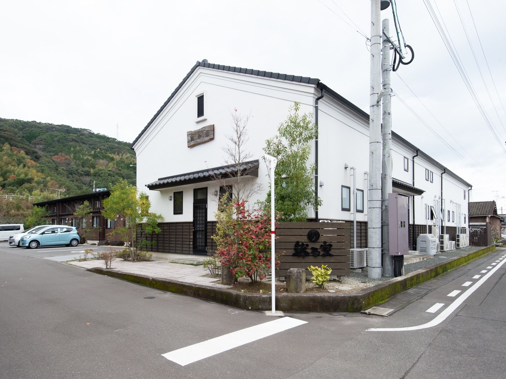 施設は2階建てで、白色の壁と木造の外壁となっている。正面には駐車スペースがあり、車が3台停められている。