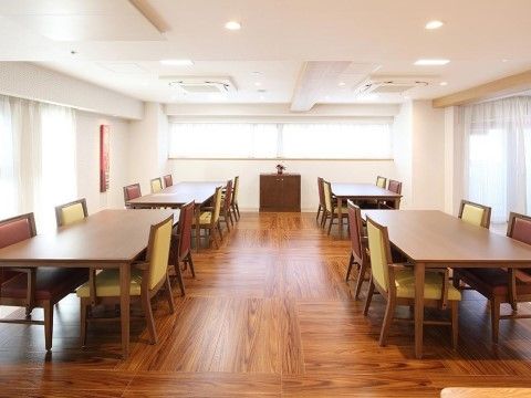 リビングには窓があり、広々とした床のスペースにはテーブルセットが間隔をあけて設置されている。床はフローリングで、テーブルと椅子は木製である。