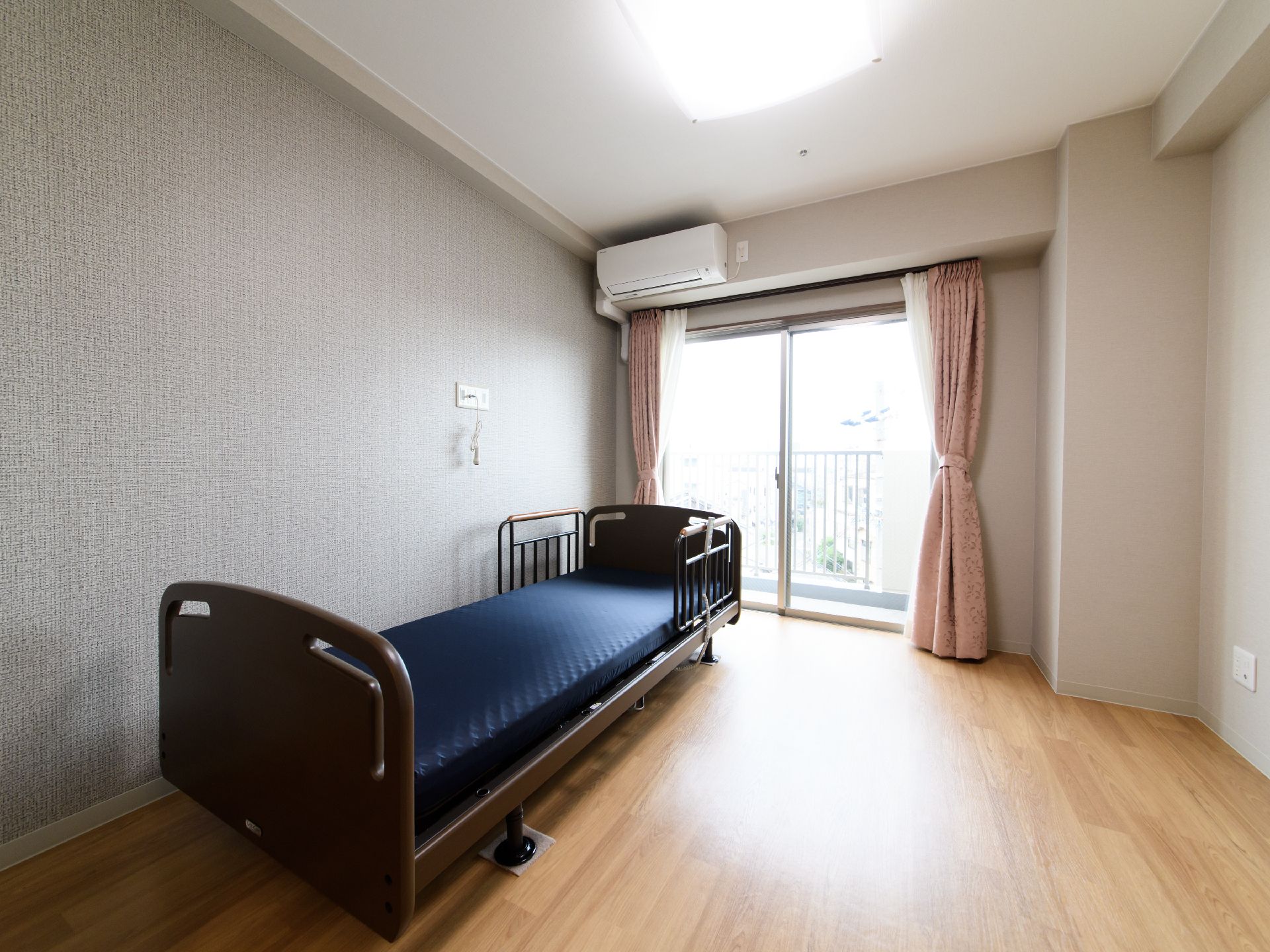 大きな窓があり、とても明るい部屋となっている。電動ベッドが置かれている。ナースコールがある。フラットの床で安全である。