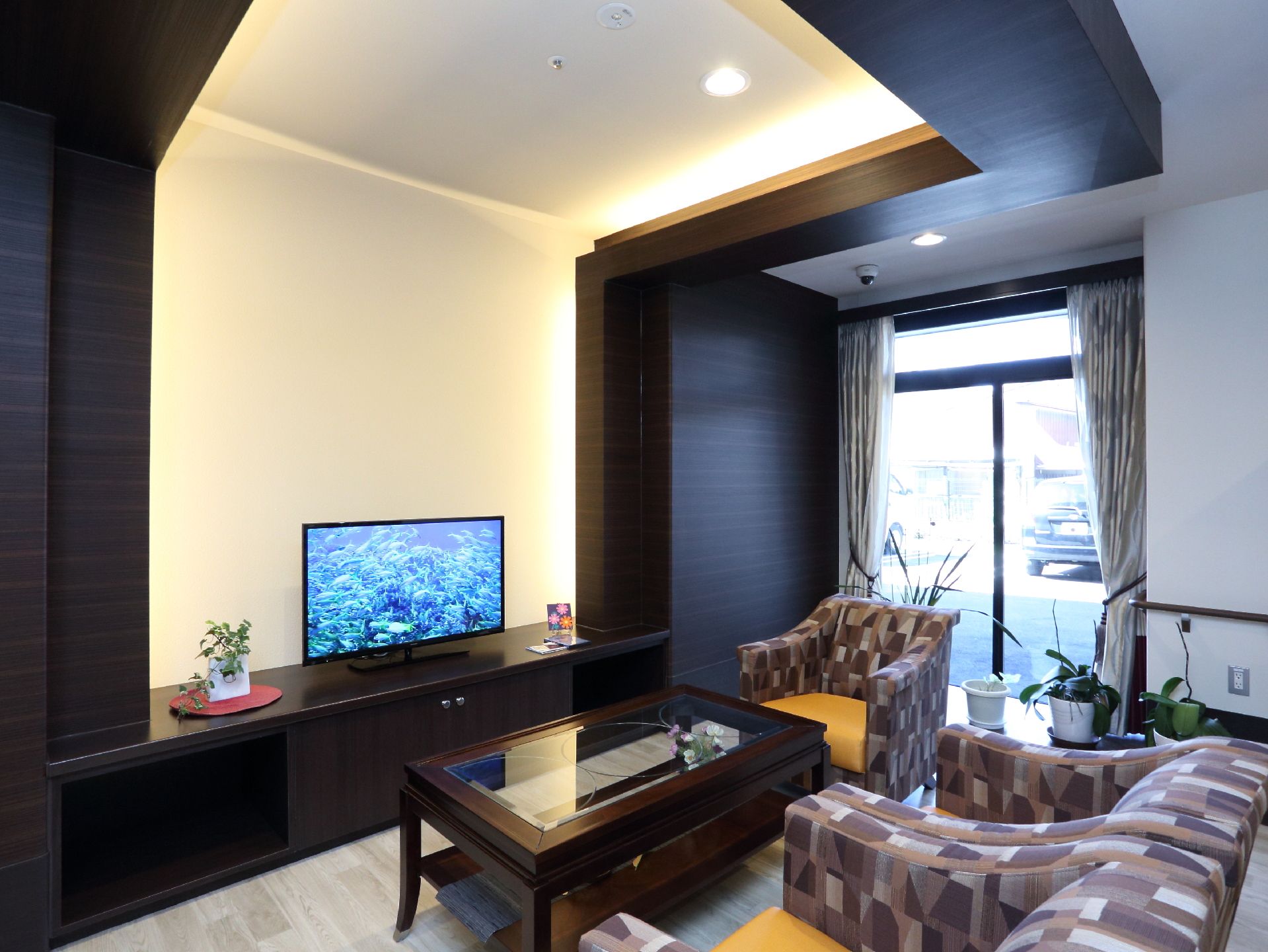ラウンジには窓があり、カーテンがついている。ボードの上にテレビが設置され、その前にテーブルとソファーなどが置かれている。