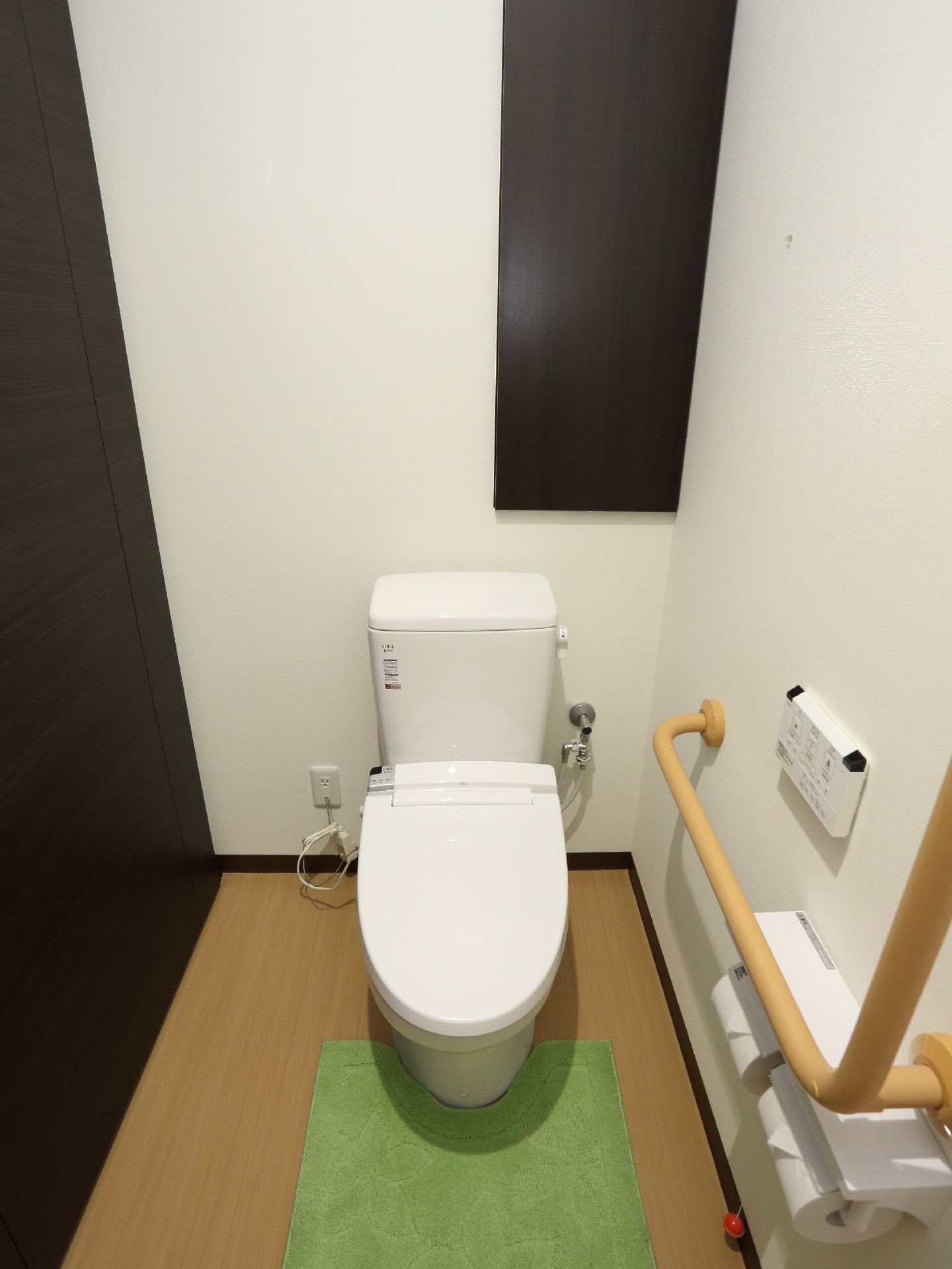 便器が中央にあり、その手前の床にはマットが敷かれている。右壁にはトイレットペーパーがある。床はフローリングになっている。