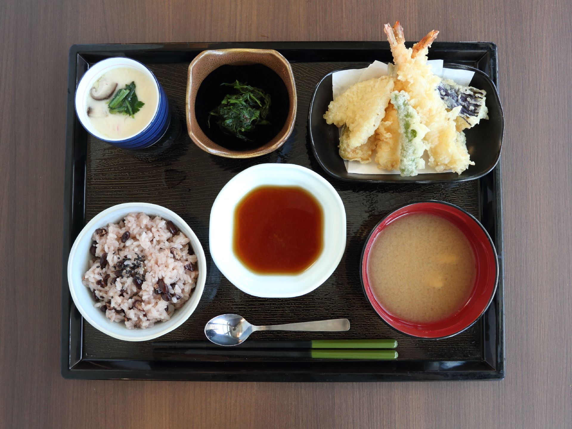 左下には赤飯がある。右下には味噌汁がある。左上には茶碗蒸しがあり、右上には天ぷらがある。そこの間にはおひたしがある。
