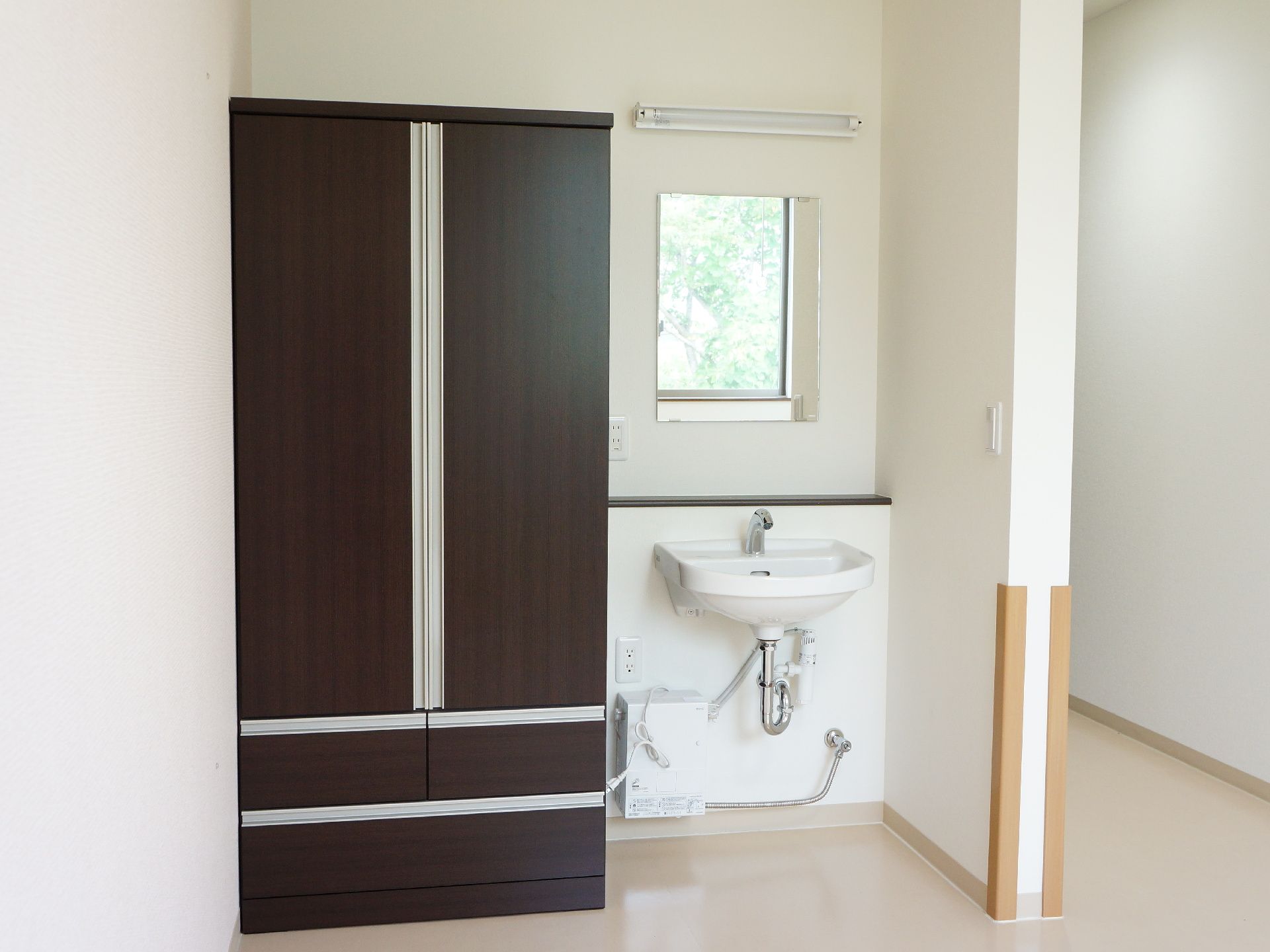 部屋に洗面台と備え付けのクローゼットがある。洗面台は車椅子でも利用しやすい形になっている。鏡や棚も付いている。
