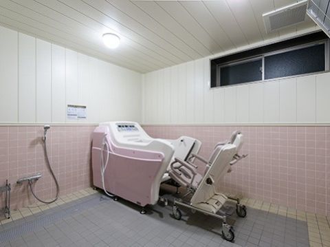ピンクや藤色のタイルを使った優しい色合いの浴室には、専用のリフトに座りそのまま浴槽に浸かる事ができる介護用の浴槽が設置されている。