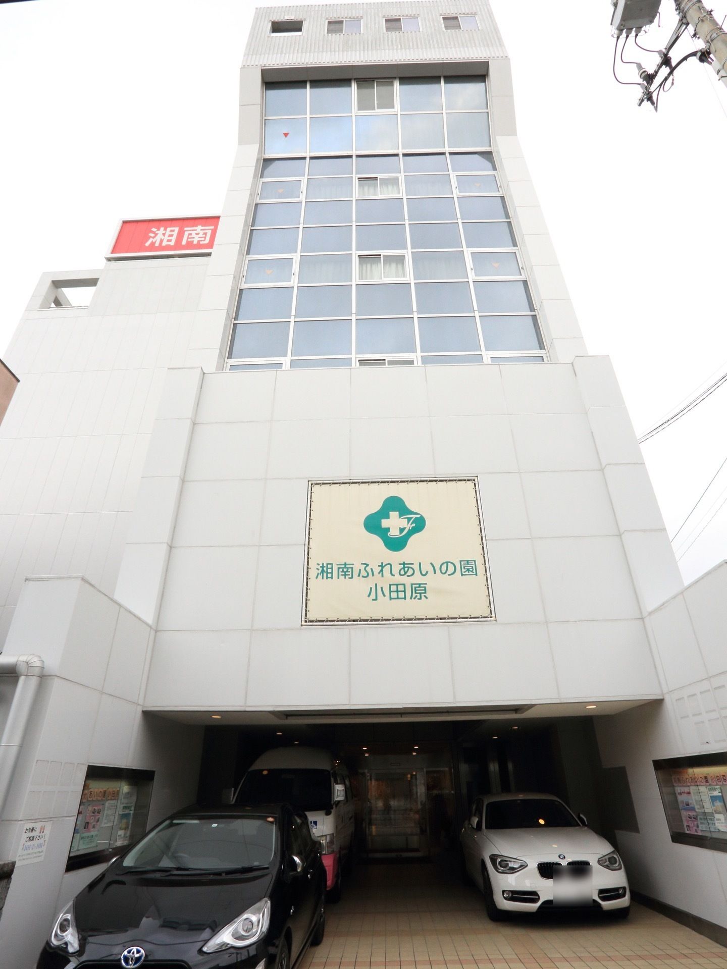 ビルのように高さのある建物である。正面の壁には、施設名称が大きく表記されている。玄関の前には、車が停まっている。