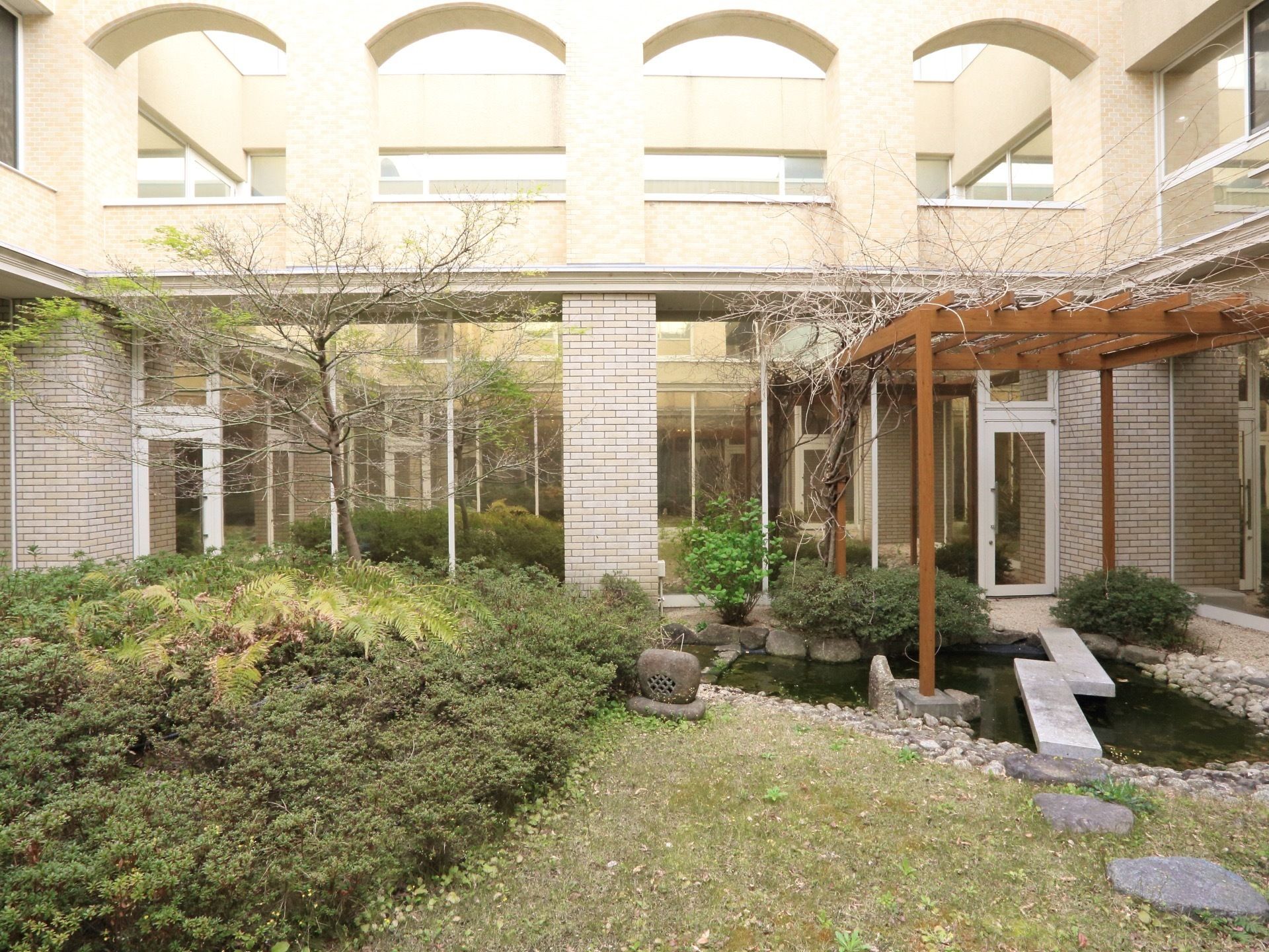 植栽と池が備わっている中庭はどの階からも眺めることができる。建物のベージュ系の色に木々の緑が美しく映えている。