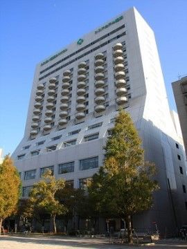 周囲に背の高い木が多く植わっている高層建ての白いホテルビル