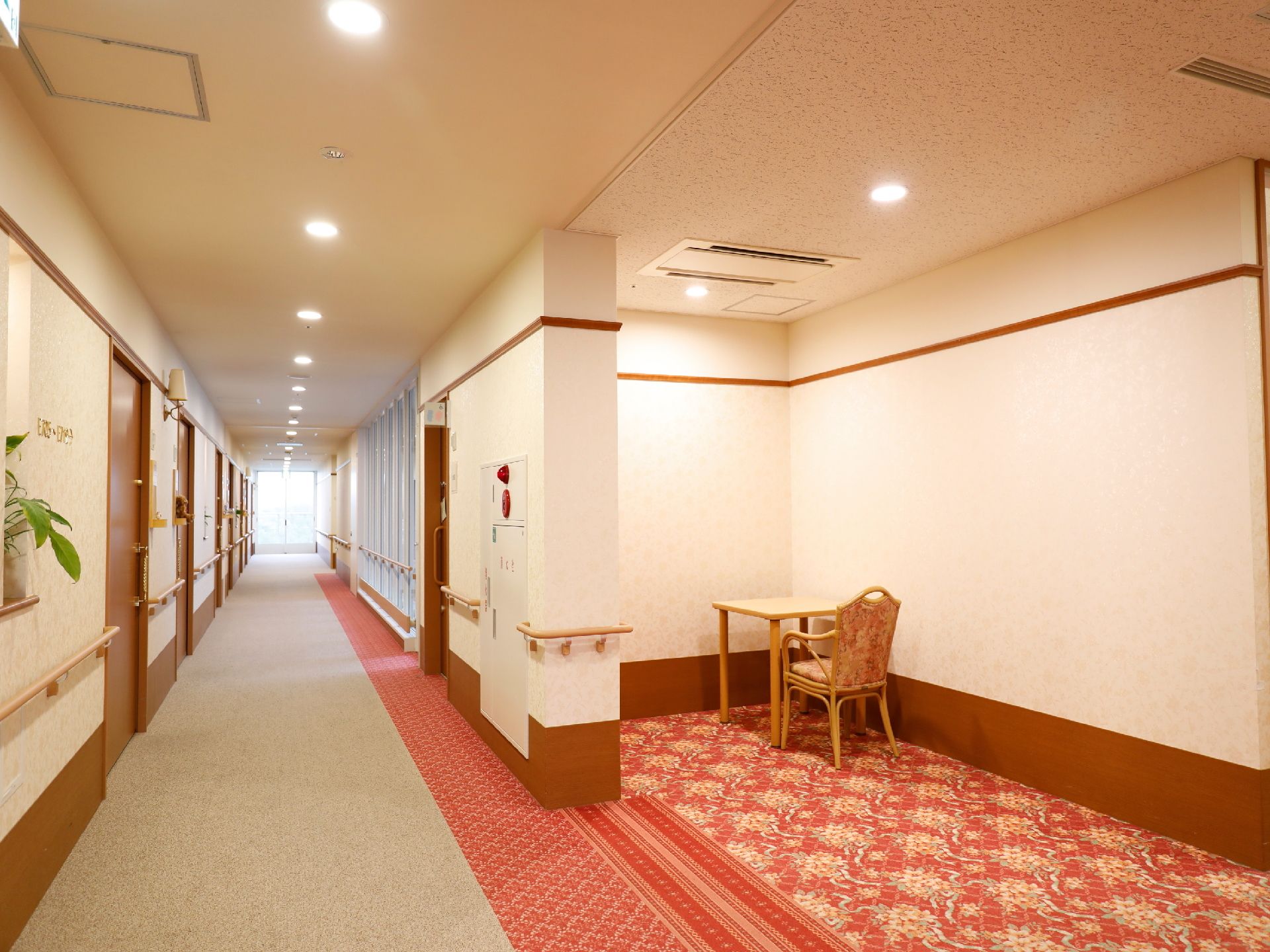 模様が施された壁と床の通路。通路に繋がっている模様入りの赤色の床スペースがある。その奥にはテーブルと一人掛けの椅子が置かれている。