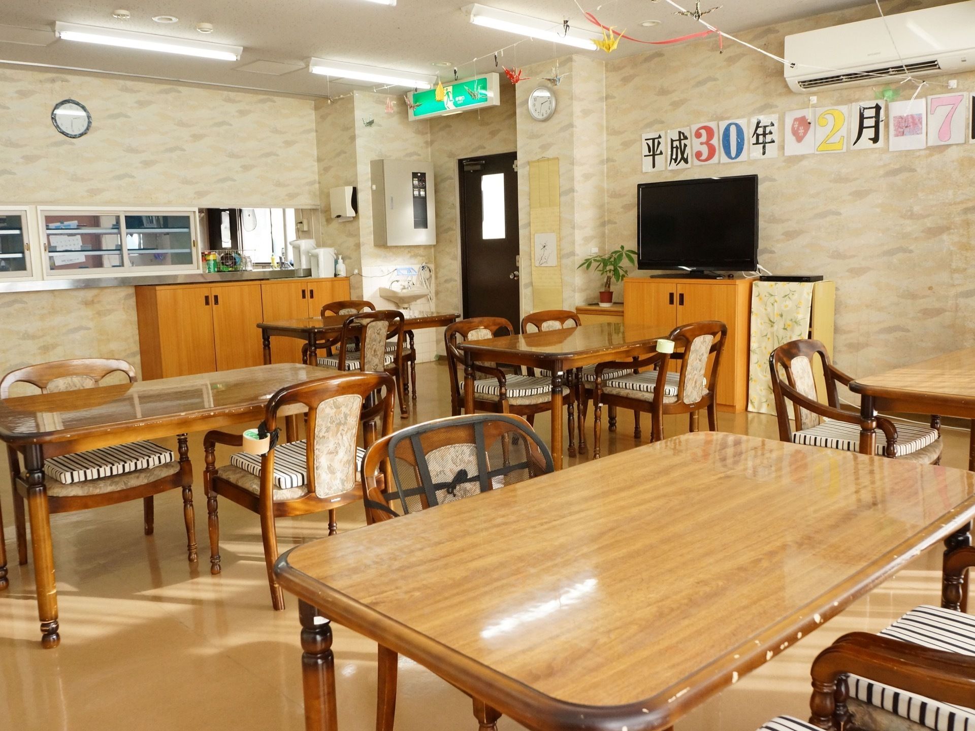 食堂に椅子とテーブルが並んでいる。壁には大きな文字で日付が表示されている。また、エアコンが設置されている。