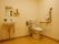 広々としたトイレで、便器と洗面台が同じ室内にある。壁にはＬ字型をした手すりと便器に設置してある温水洗浄機能のボタンがある。