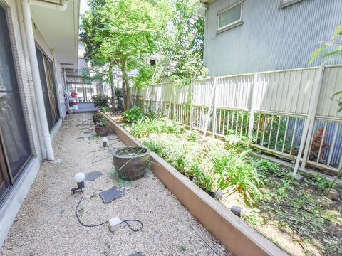 木や花などの植物を植えた花壇がある。大きな植木鉢や敷き石がある。隣接した建物とも十分な距離がとってある。