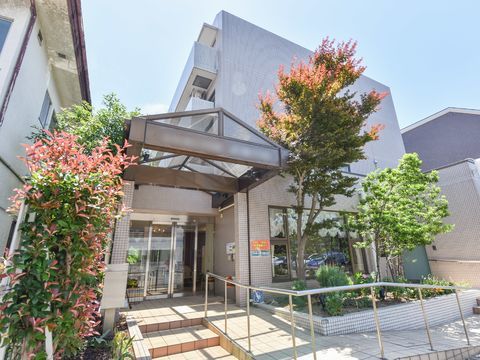 周囲に木などの植物の花壇がある。玄関前にスロープと階段がある。正面ドアは自動でガラス張りの造りである。