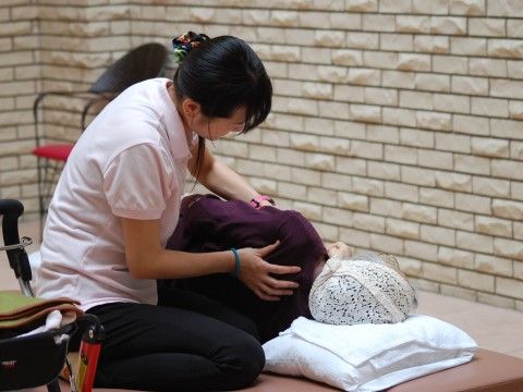寝転がったご入居者様の肩をマッサージしているスタッフ