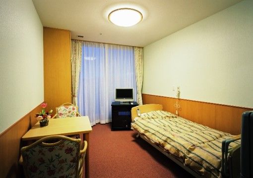 居室の内装は、白い壁と茶色の板を敷き詰めた壁とに分かれ、上下のカラーが異なっている。ベッドのそばには、ナースコール用のコードが出ている。