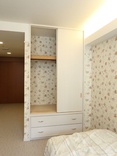 花柄の壁の仕様の内装に白色のクローゼットが置いてある。内部の正面も花柄、洋服を掛けの上は棚になっていて、下は2段の引き出し。