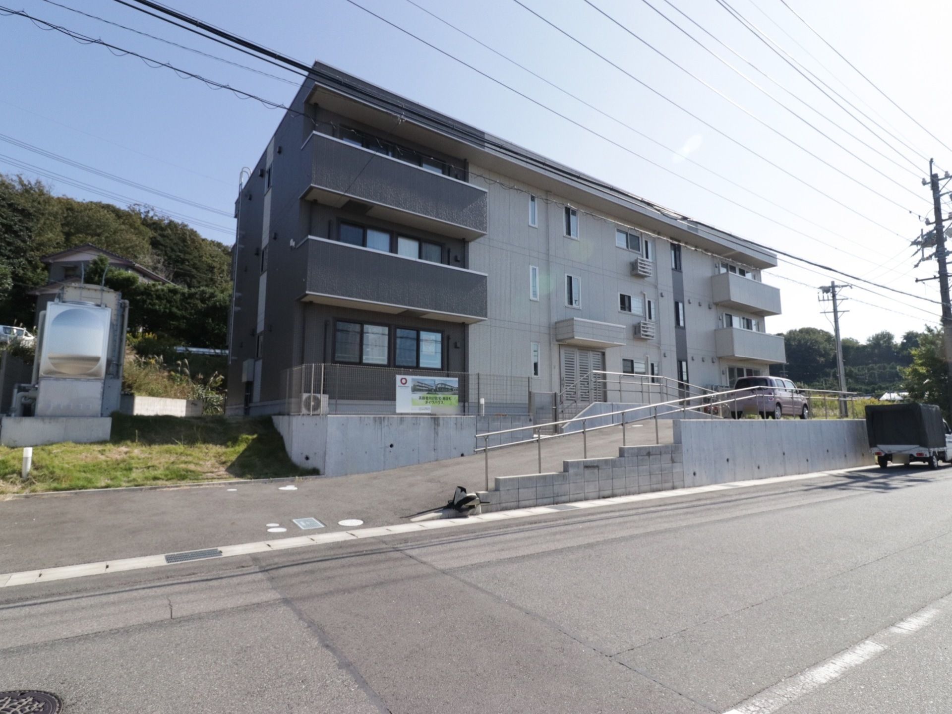 施設の建物は三階建てで、上階にはベランダを設置している。前面には駐車スペースがあり、玄関へと続くスロープに手すりを取り付けている。