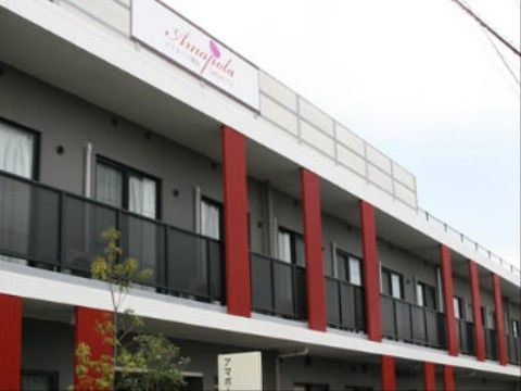白とグレーの外壁に赤の支柱が印象的な、鉄筋コンクリート造２階建ての建物。屋上に大きく施設の看板が立てられている。
