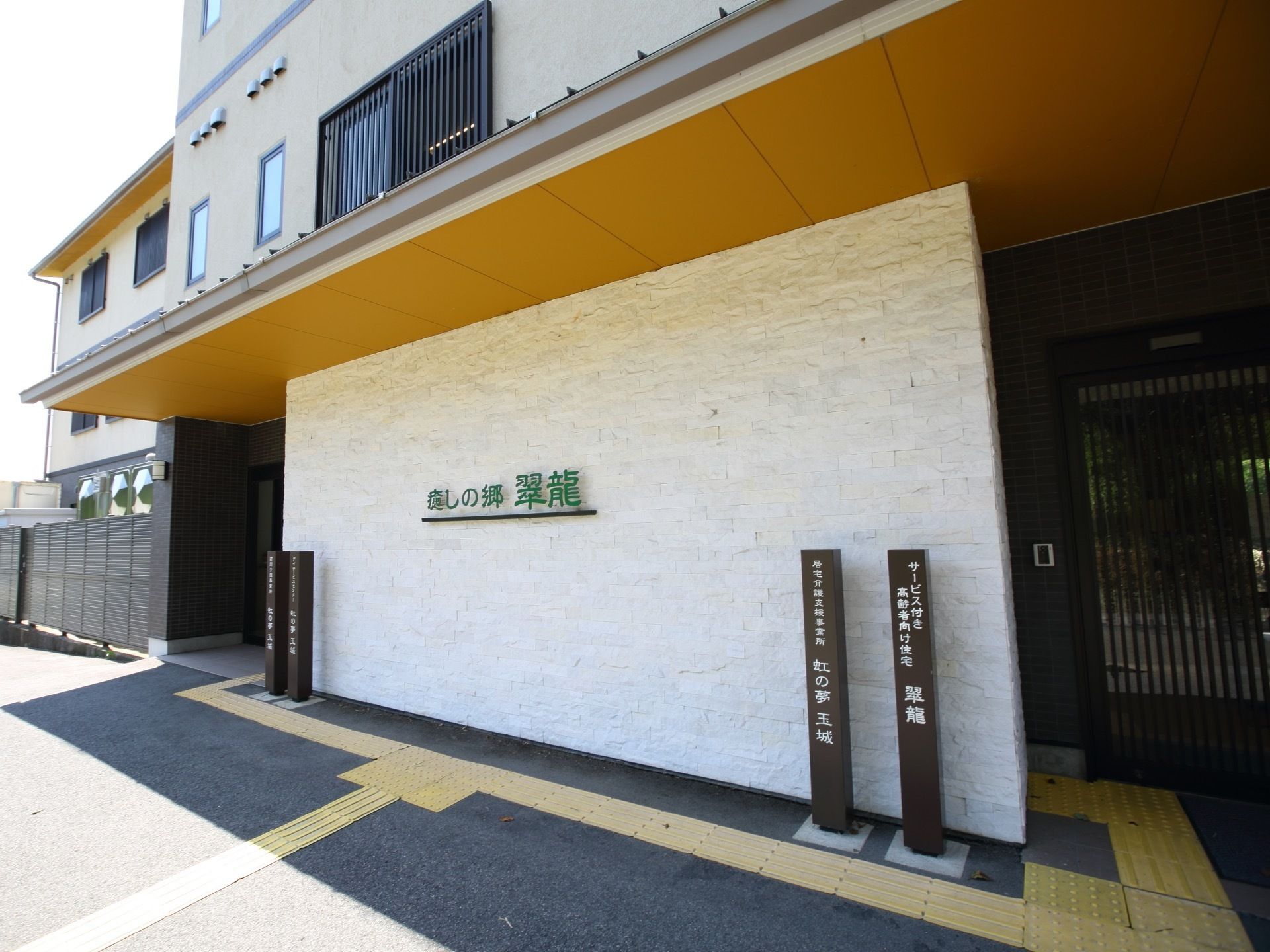 大きく横長のひさしが付いたエントランスである。壁には、施設名が大きく記されている。出入り口が２つ設けられている。
