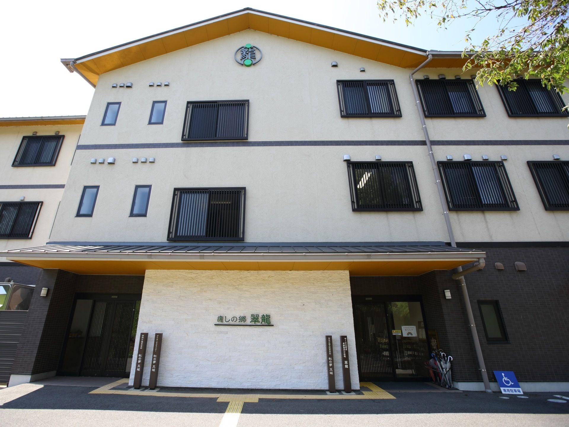 温泉旅館のような外観の３階建て施設である。ひさし付きのエントランスには２つの出入り口が設けられている。