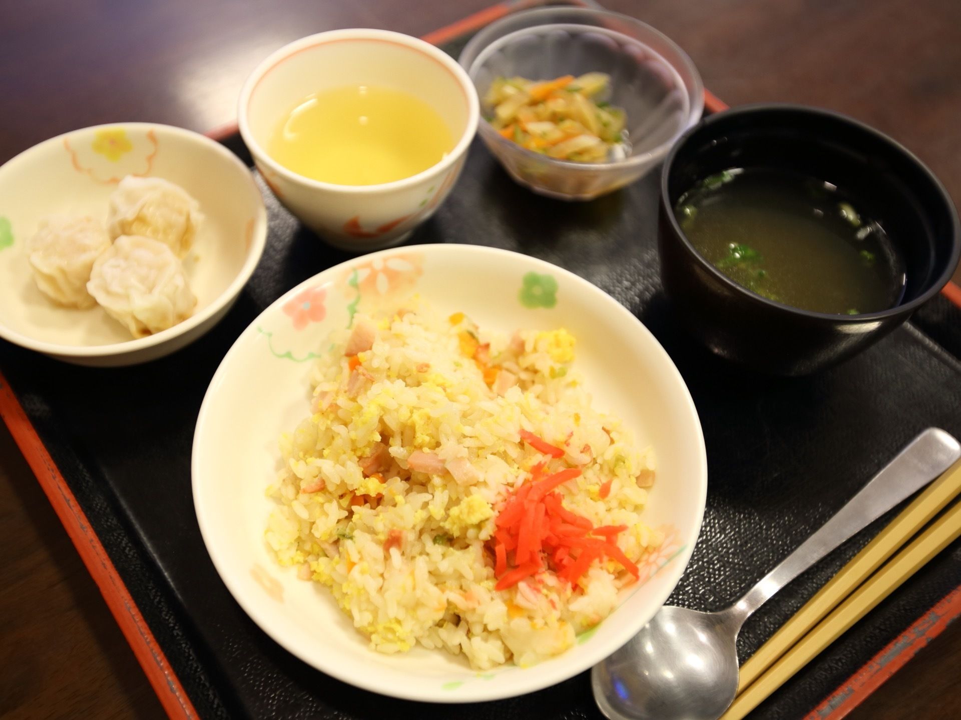 黒いトレイには、チャーハンやシュウマイ、スープなど中華風のメニューが並べられている。スプーンと箸を用意。