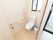 トイレの入口は引き戸になっている。便座の横に掃除道具やごみ箱が置かれている。タオルハンガーにピンク色のタオルがかかっている。