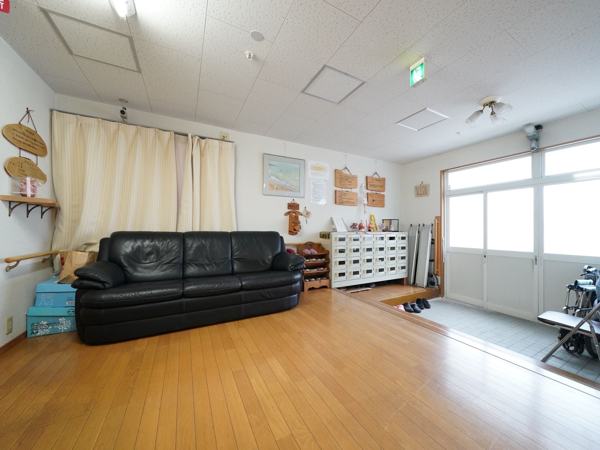 大きな黒いソファがある。下駄箱とスリッパ置き場が用意されている。たたきには車椅子と椅子が置かれている。