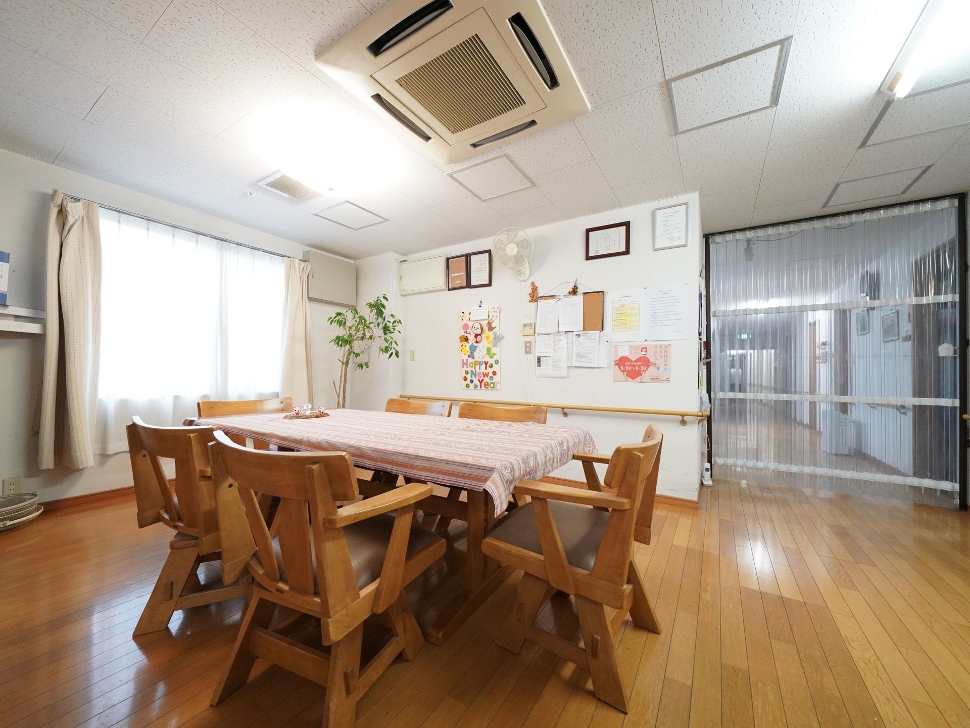 リビングには、テーブルに回転式の6脚の椅子が設置されている。廊下との間仕切りに見通しの良い透明ビニールのが掛けられている。