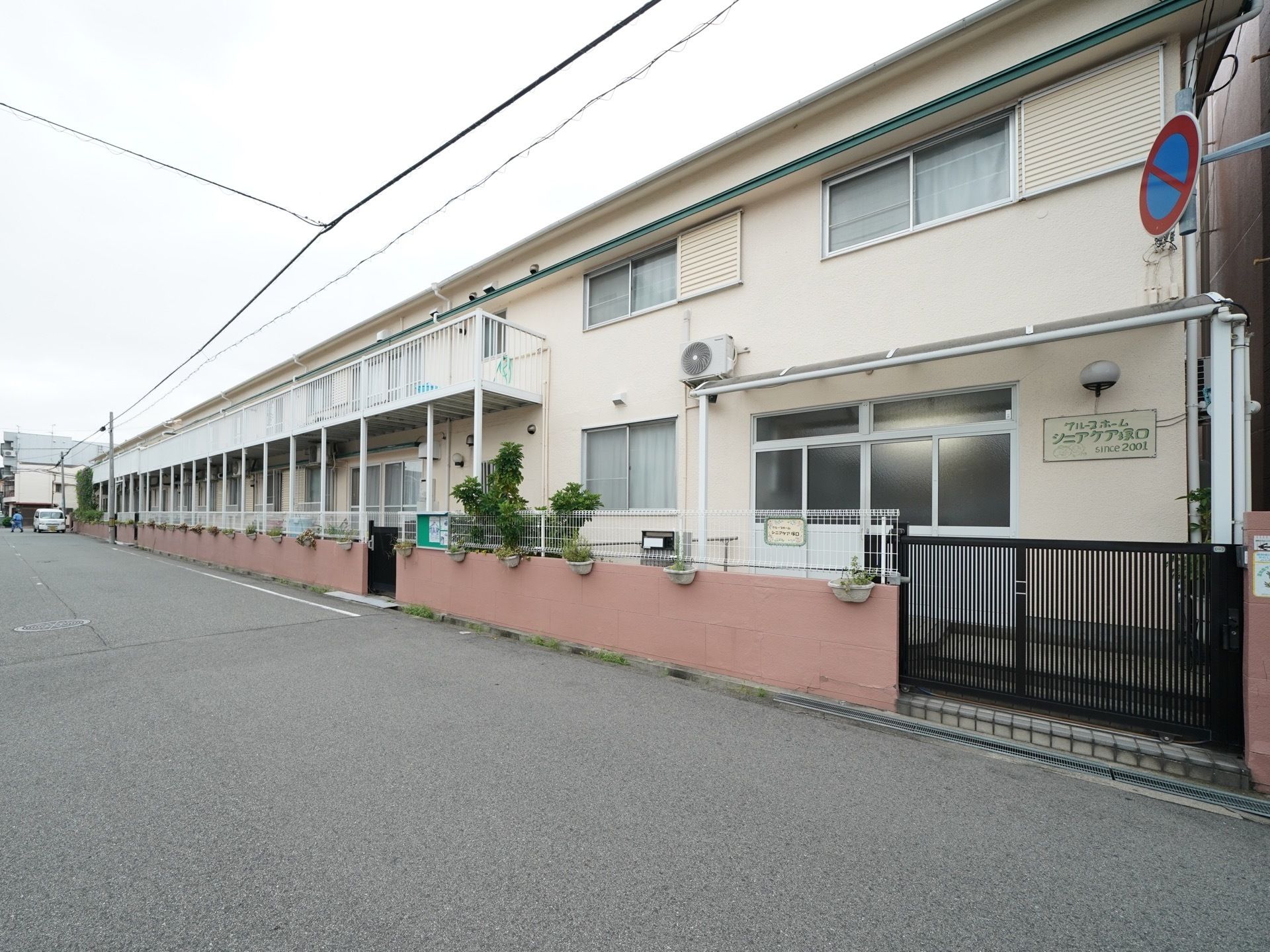 大きな道路に面している。玄関には屋根がついている。引き戸門扉が設置されている。２階建ての白い建造物である。