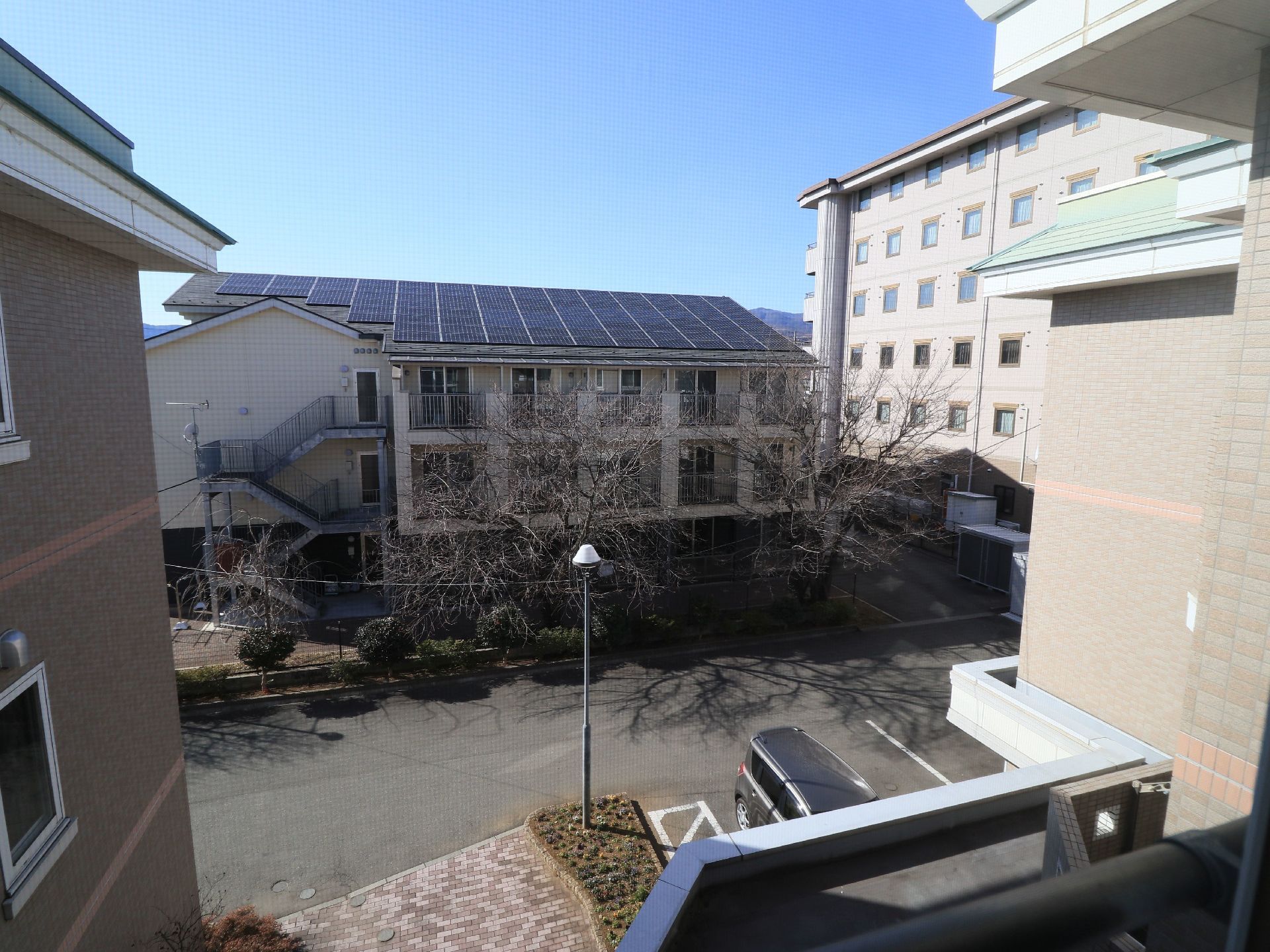 落ち着いた色合いのマンション風の施設外観になっている。敷地内には駐車場が完備されており、車が１台停まっている。