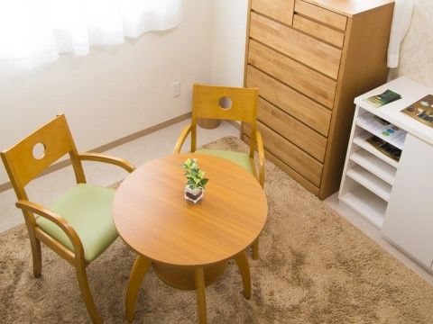 毛足の長いカーペットの上には丸テーブルに２脚の椅子、壁際には箪笥と白い棚が設置されている。自宅のように落ち着ける空間になっている。