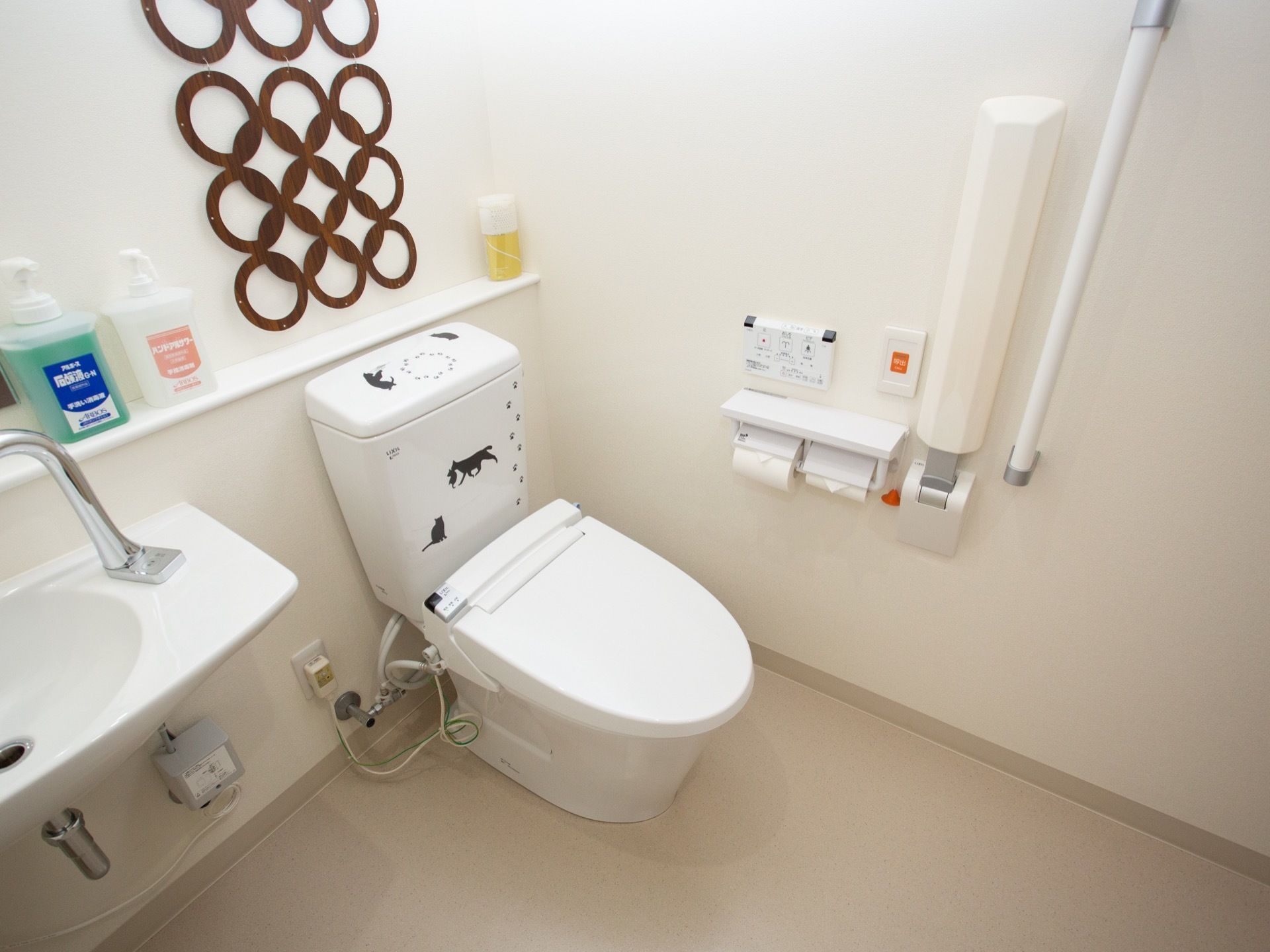 トイレのタンクに猫を型取ったステッカーが貼られている。壁面には縦型と折りたたみ式の手すりが取り付けてある。