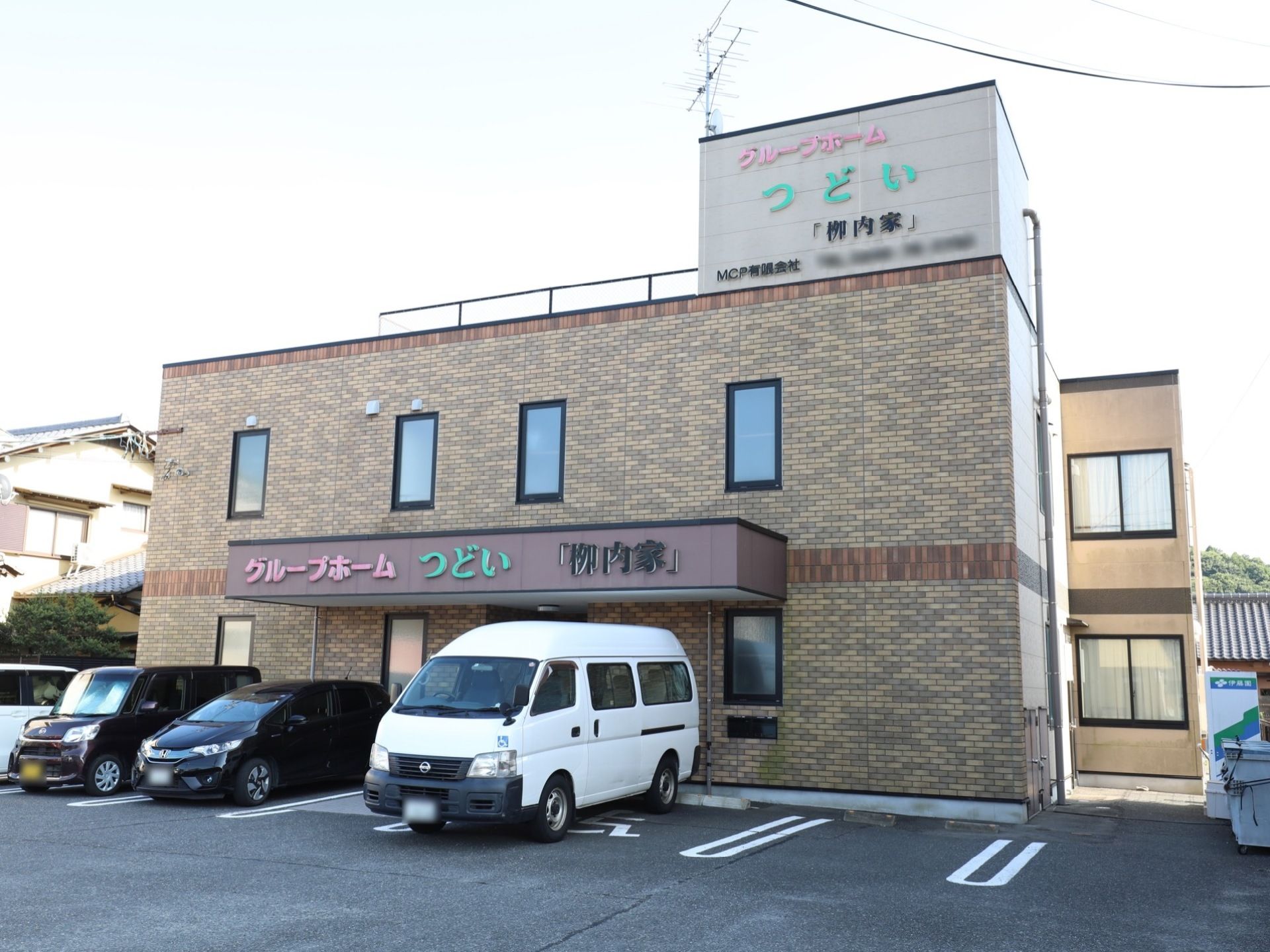 ２階建てのグループホームである。車椅子をご利用の方専用の駐車スペースに、白いワゴン車が停められている。