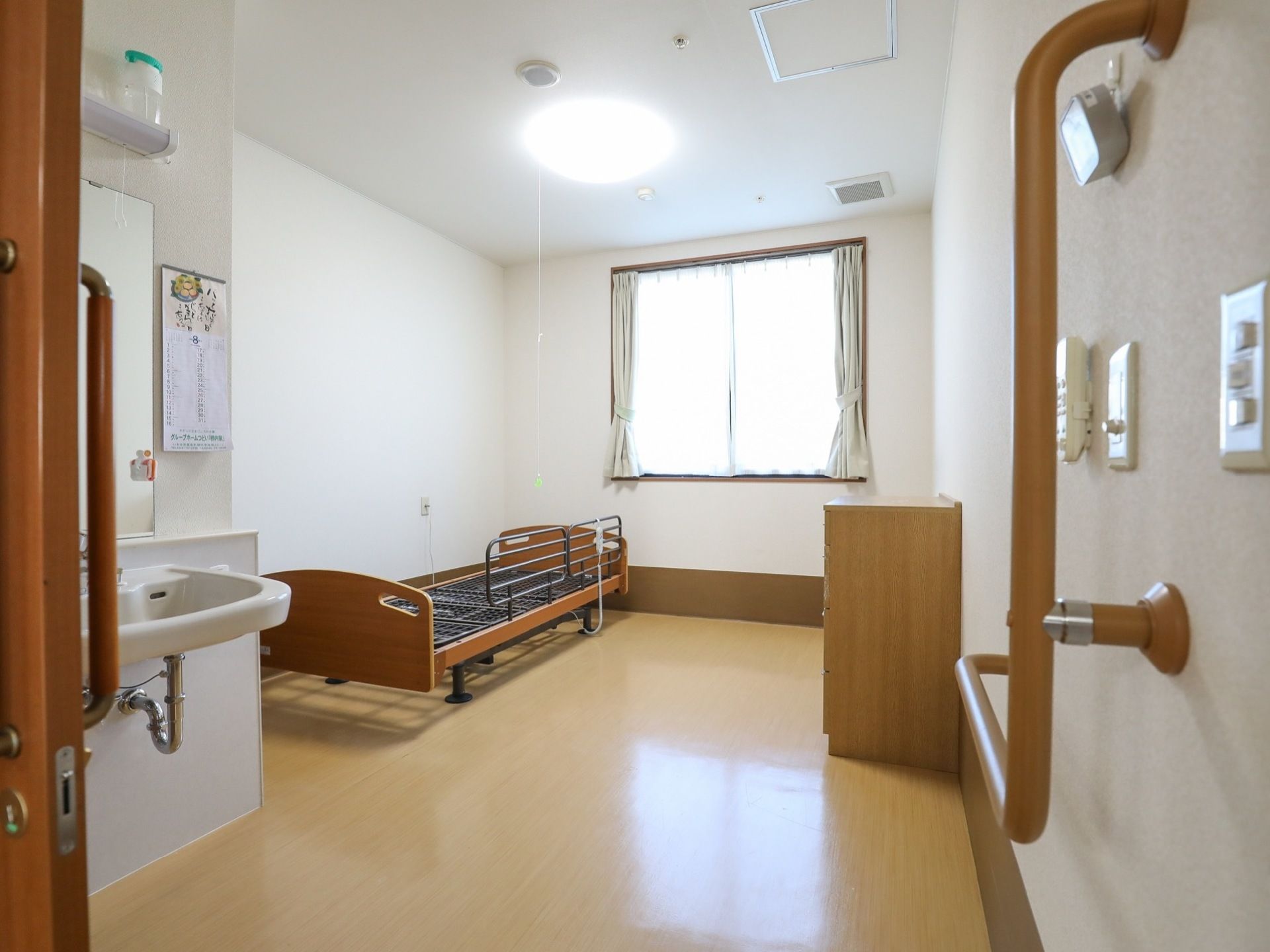 介護ベッド横の壁にはナースコールが設置されている。天井に照明が、窓にはカーテンが取りつけられている。