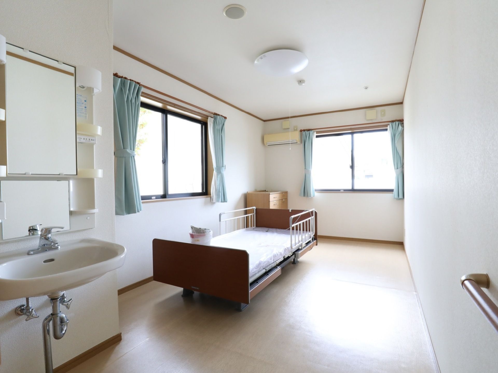 角のお部屋には、窓が２セットついている。入口側の壁には、手すりが設置してあり、反対側に洗面所もついている。