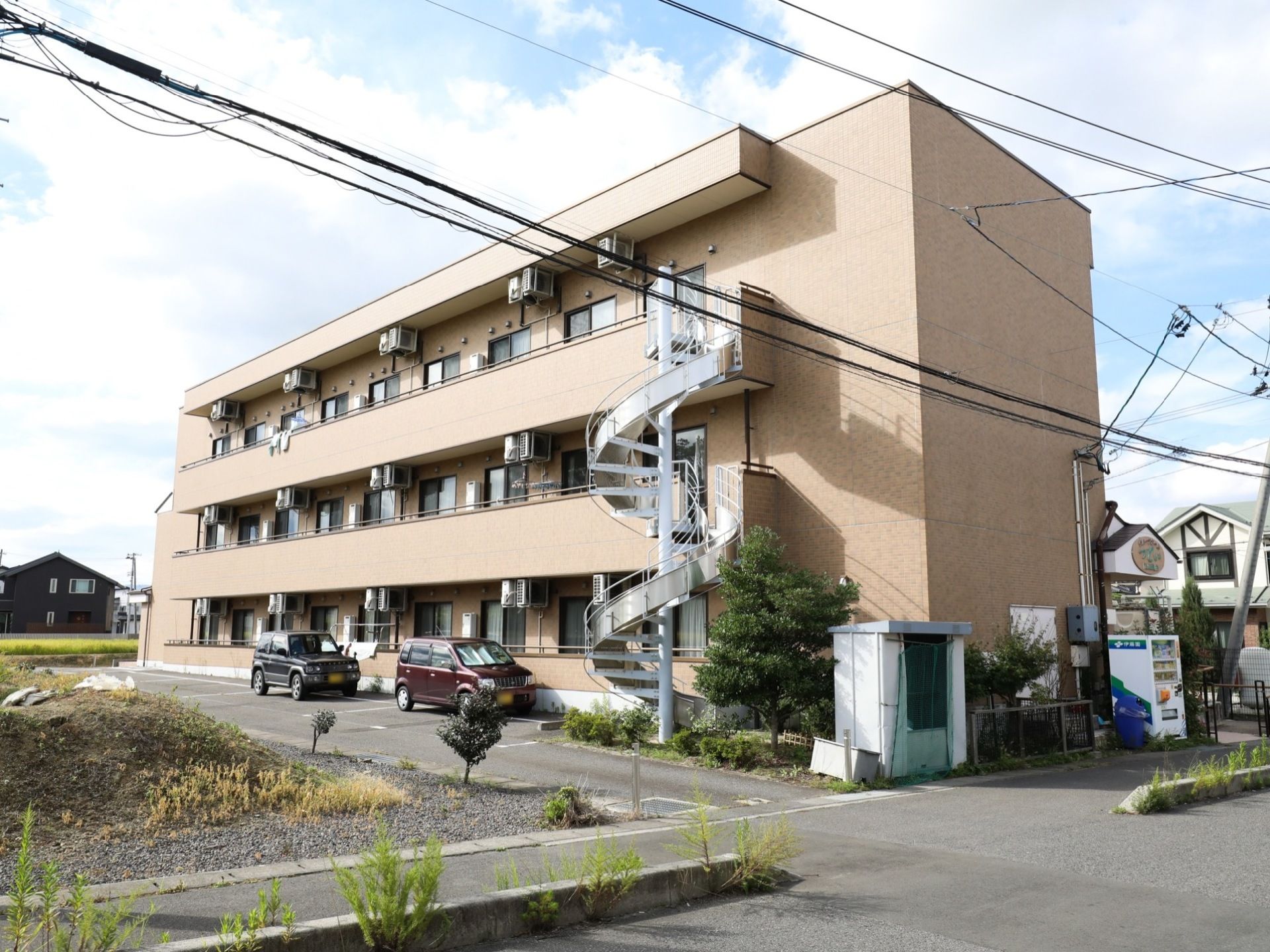 塀がなく開放的な広い敷地に建っている施設建物は３階建てで、各階にはベランダ付きの同形同色のガラス戸が設置されたマンション風の外観である。